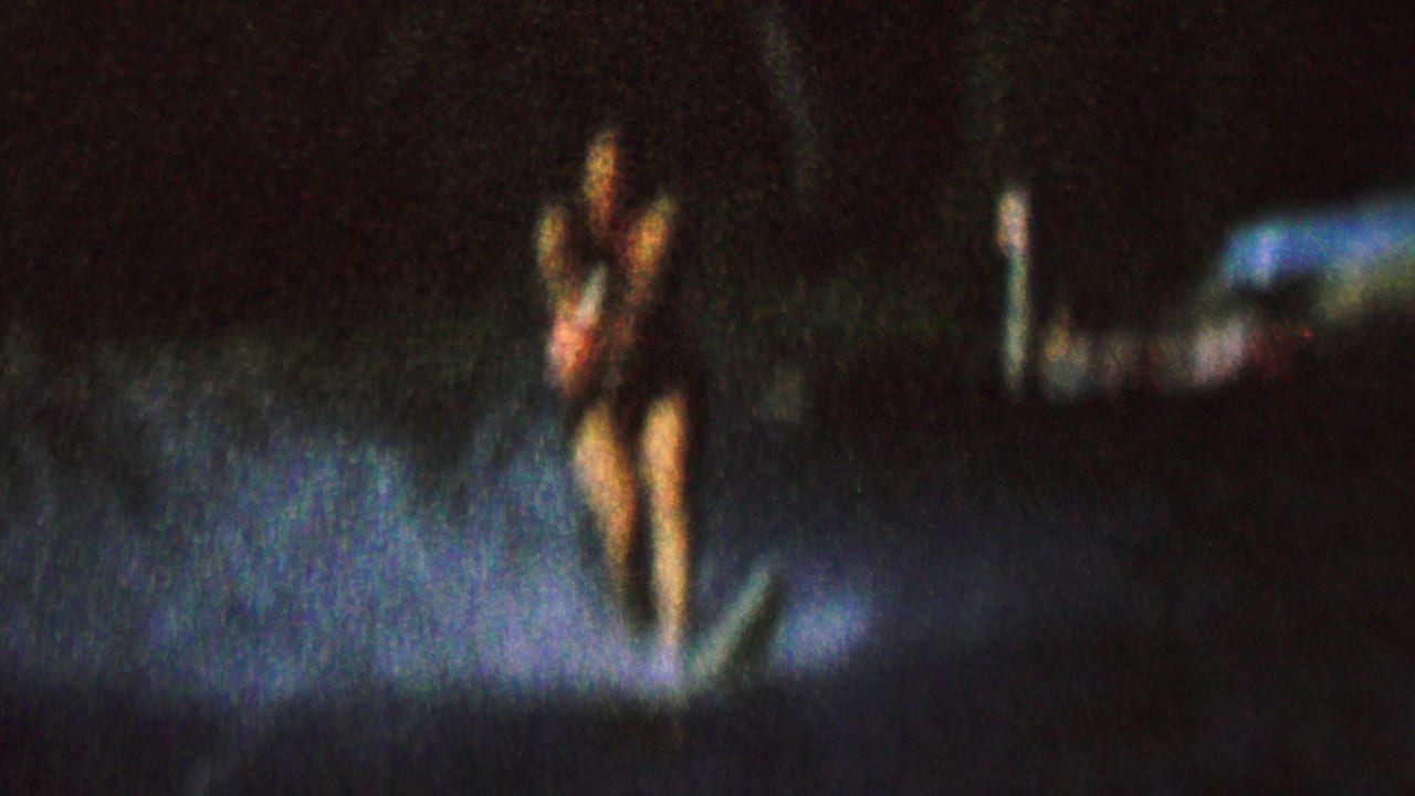 A woman on water skis moves across a night lake, with blue-white light catching the spray and trees barely visible behind her.