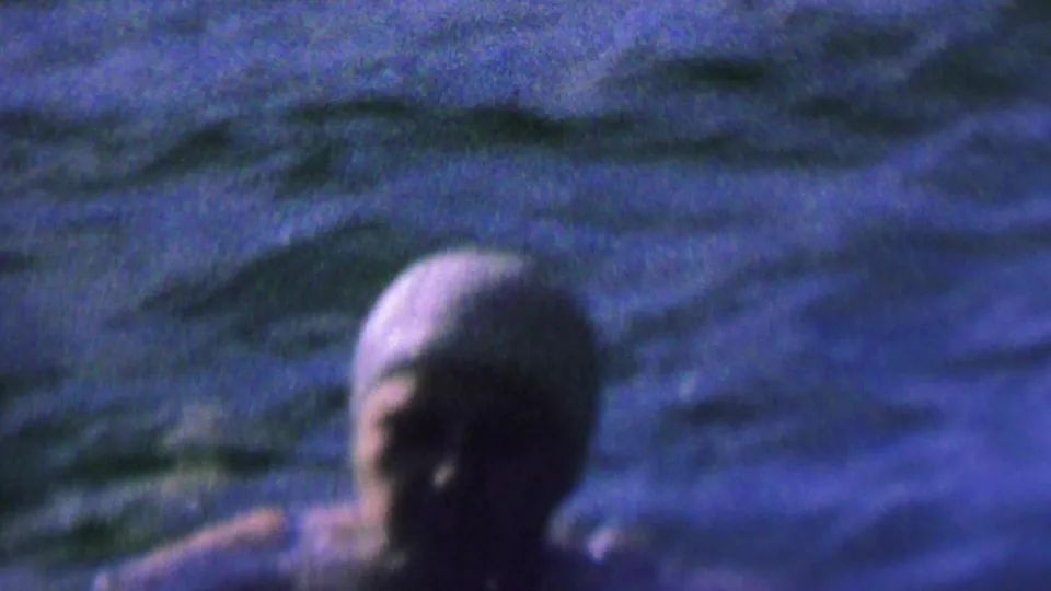 Soft 8mm frame from the 1962 lake scene showing a swimmer close to the camera with head and arm above rippling water.