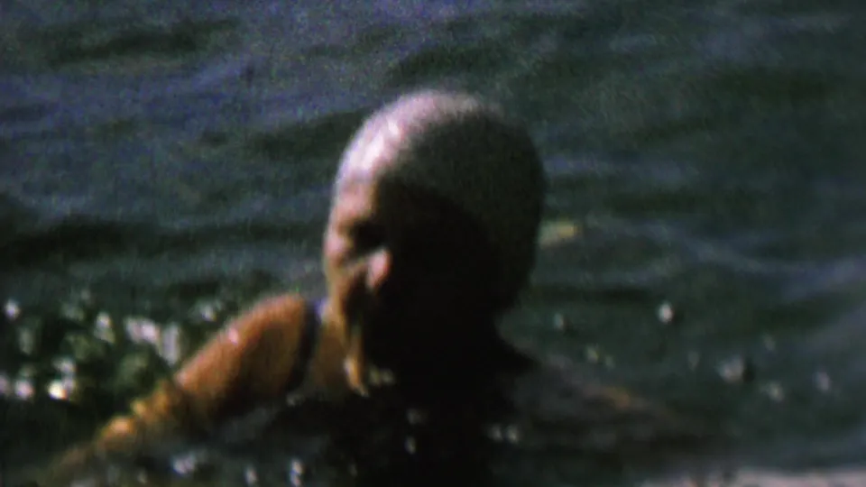 1962 home-movie frame showing a swimmer's head and shoulders in the lake, with the face partially visible amid grain and shadow.
