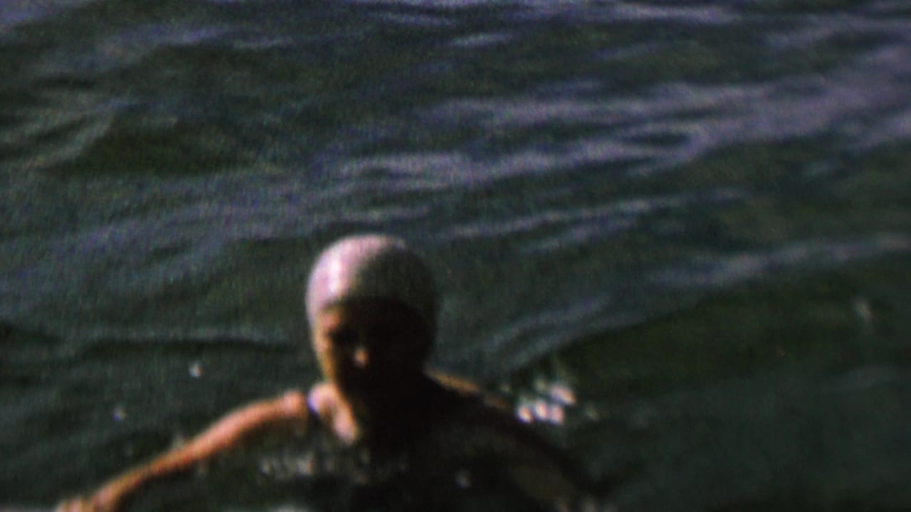 A light-capped swimmer moves through dark rippling lake water in metadata-supported 1962 St. Paul, Minnesota 8mm home-movie footage.