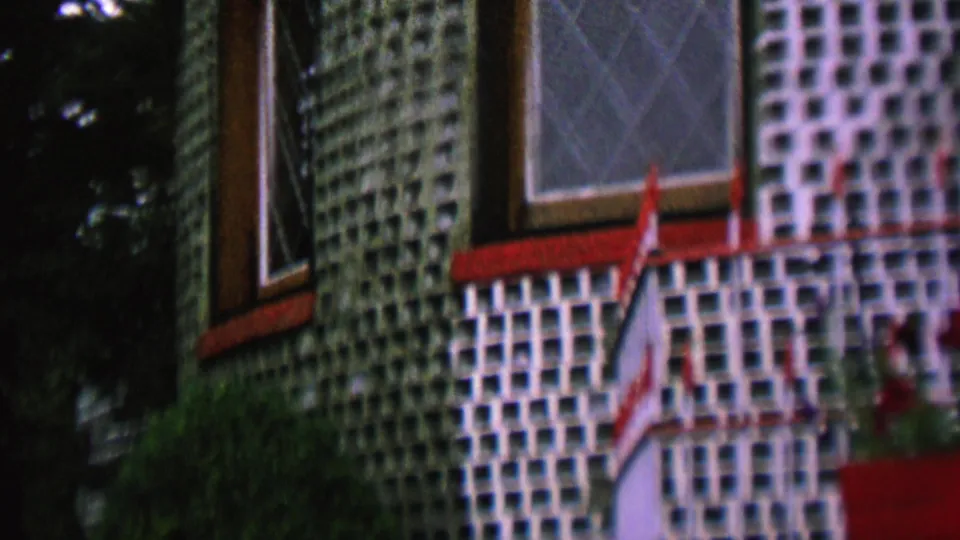 Final frame of the 1962 St. Paul clip holds on the distinctive glass-bottle house wall, with red-trimmed windows and foliage partly obscuring the exterior.
