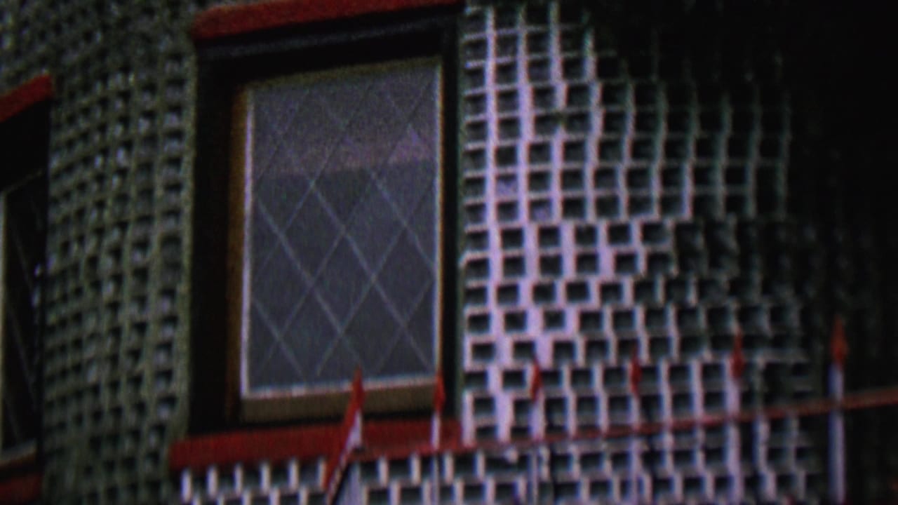 1962 St Paul home-movie frame of a decorative tiled building exterior with a diamond-paned window, red trim, and shadowed facade sections.