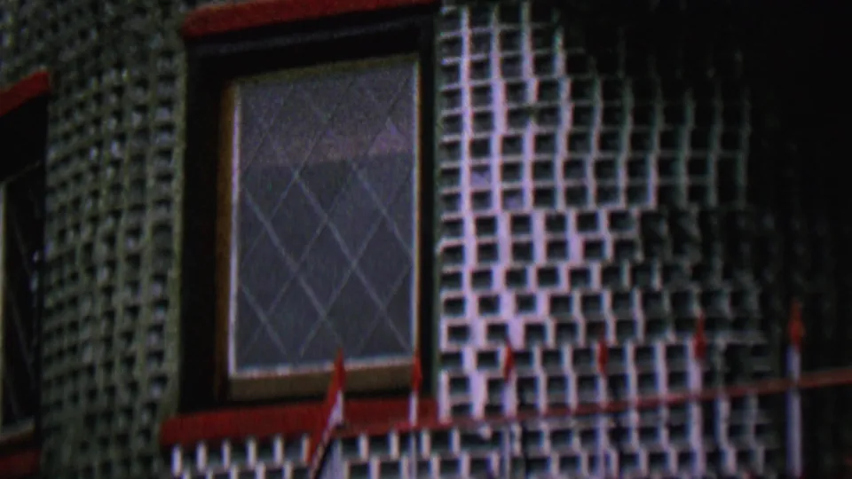1962 St Paul home-movie frame of a decorative tiled building exterior with a diamond-paned window, red trim, and shadowed facade sections.