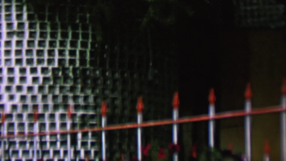 1962 St Paul exterior frame with decorative grid-pattern tilework, dark foliage, a fence line, red-tipped posts, and small red accents near the base.
