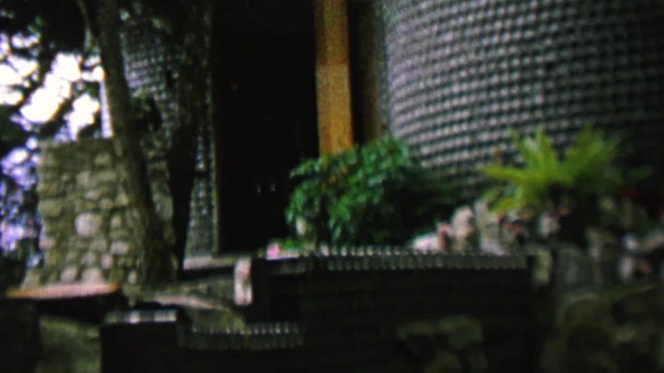 Garden-side view of a textured stone-covered building facade or entrance area, with a low wall, plants, and trees in 1962 St. Paul footage.