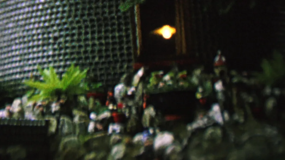 Final frame of the 1962 St Paul home-movie clip showing plants on a ledge, a textured grid wall, vertical trim, and a small warm light near a dark exterior entrance.