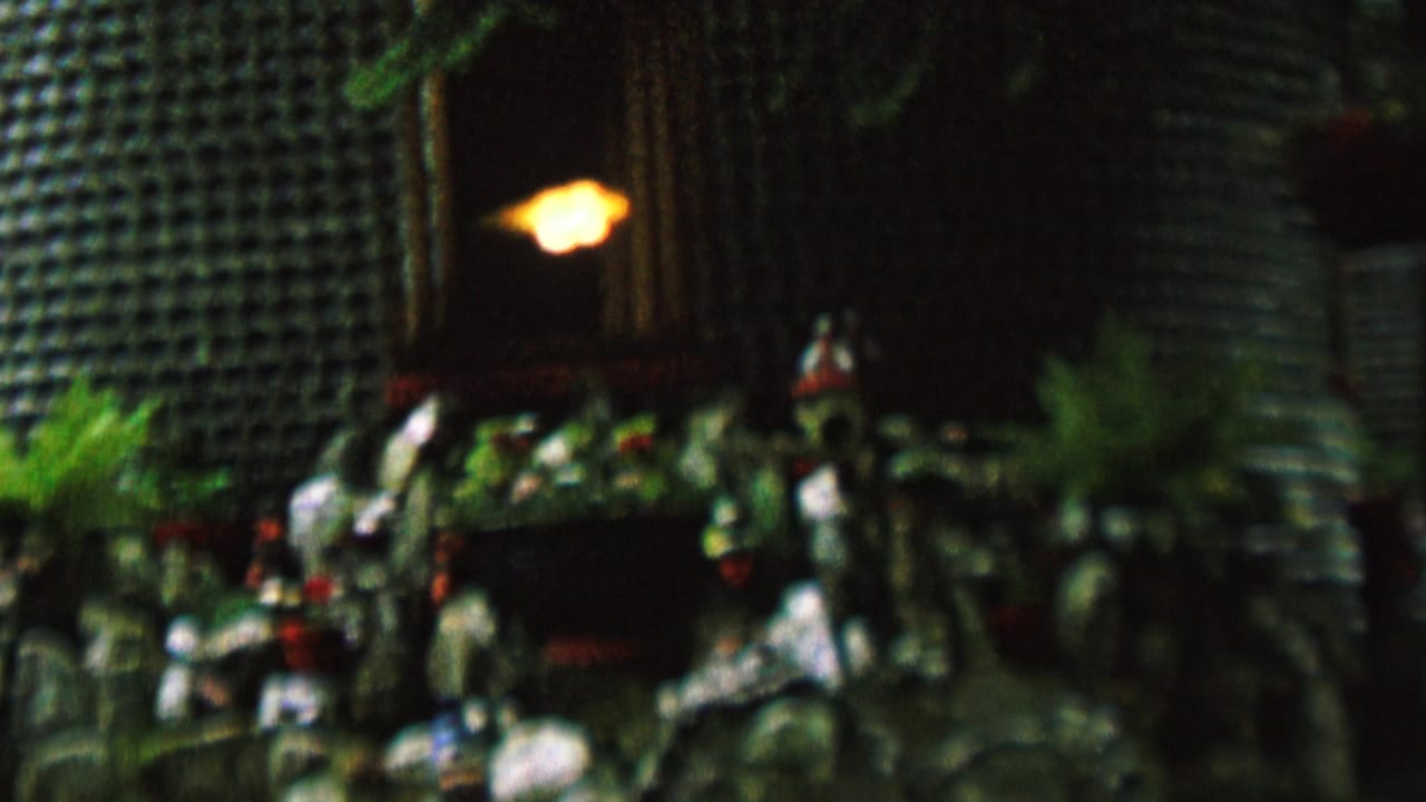 1962 8mm home-movie frame from St. Paul, Minnesota, showing a soft-focus decorative garden or memorial display with stacked bottle texture, figurines, greenery, and a warm light.
