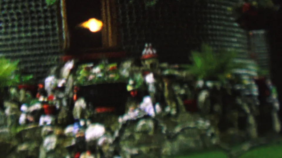 1962 St. Paul 8mm frame showing a decorative garden or memorial installation in soft focus, with stacked bottle texture, clustered figurines, planted greenery, and a warm illuminated recess.