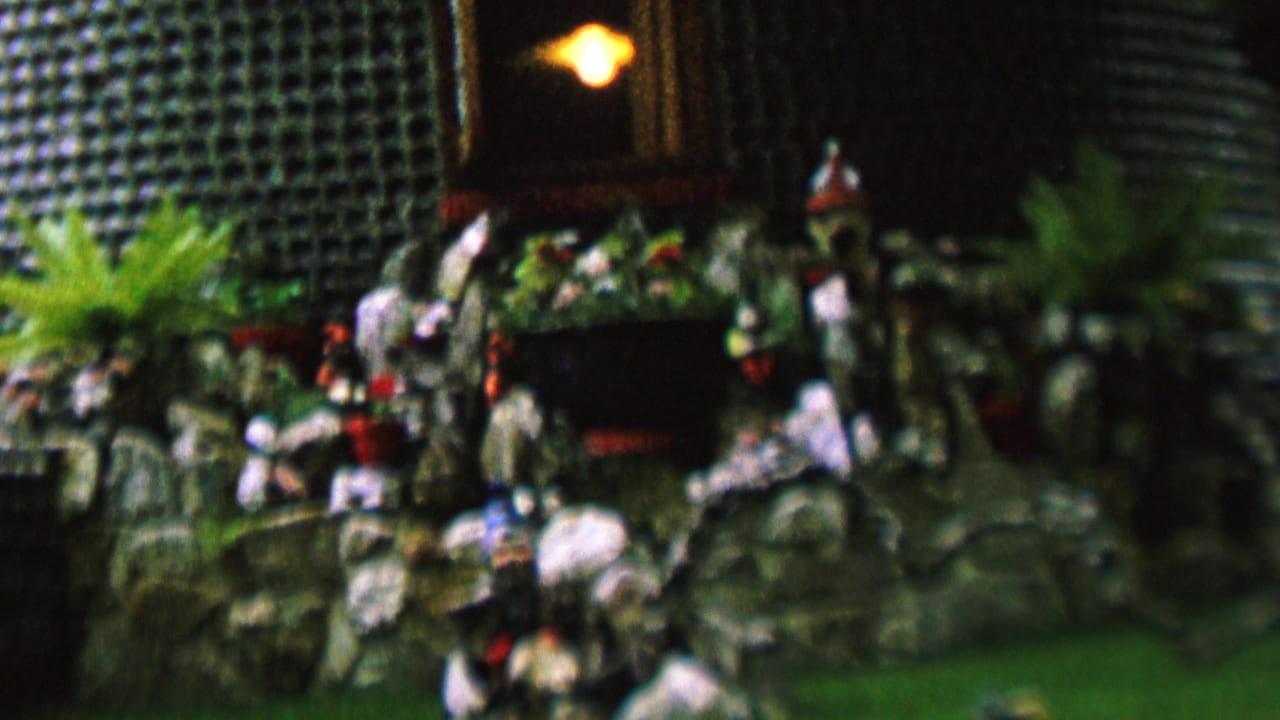 1962 8mm frame from St. Paul, Minnesota showing a miniature rock garden diorama with small figurines, potted plants, greenery, and a warm light above the display.