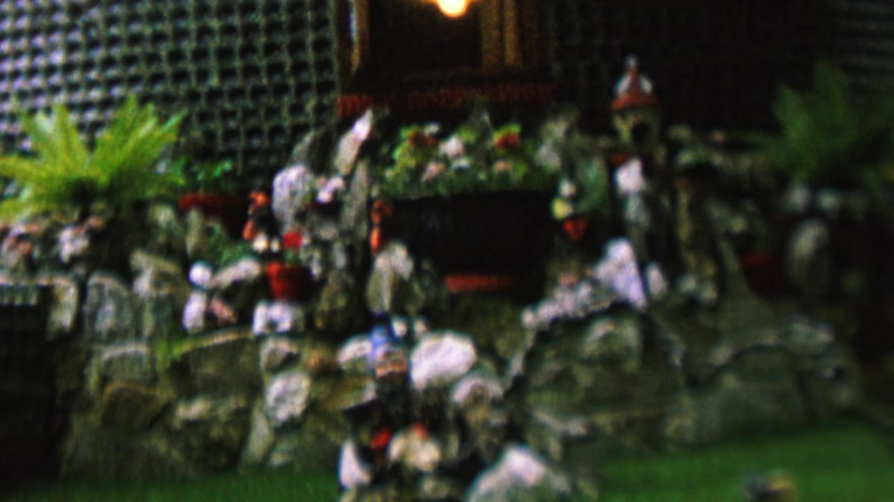 Miniature garden scene with rocks, plants, figurines, and a dark backdrop.