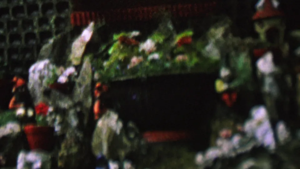 The final frame emphasizes the right side of the miniature rock garden, where a bird-like decorative figure, potted greenery, small figurines, and a dark recessed structure are visible.