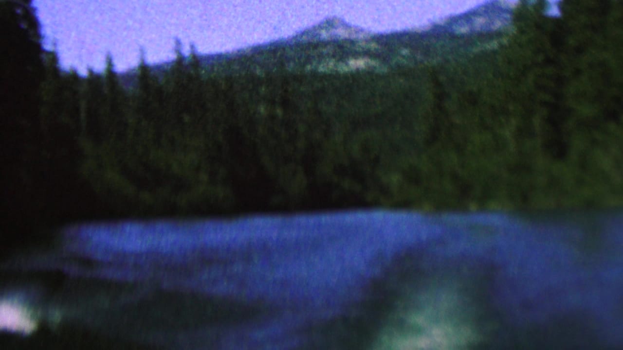 Lake surface with dark forested shoreline and hazy ridges beyond.