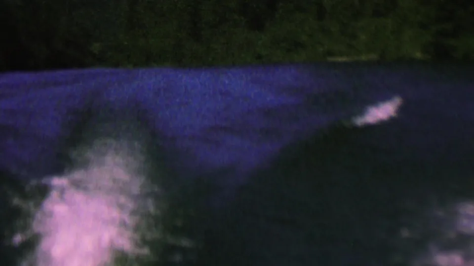 Final 1962 home-movie frame of dark lake water and a pale motorboat wake, with the distant St. Paul shoreline suggested by shadowed trees in the background.
