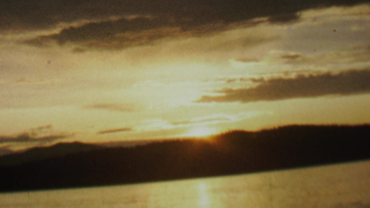 Golden sunrise reflected on lake water beneath dark clouds.