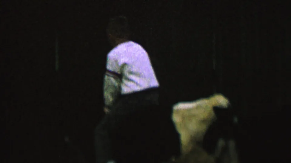 In 1962 home-movie footage identified as St. Paul, Minnesota, a small rider seen from behind sits on a light-colored cow against a nearly black background.