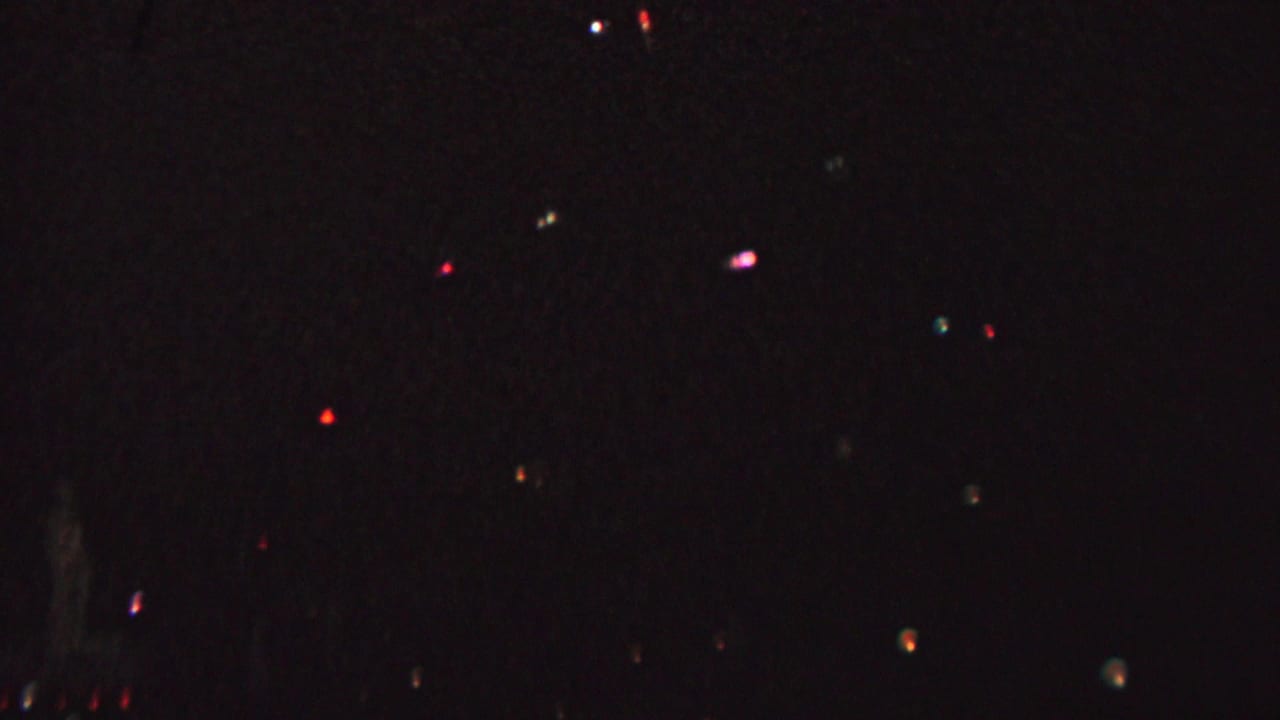 Dark frame with distant colored lights and a small bright light near the center lower area.