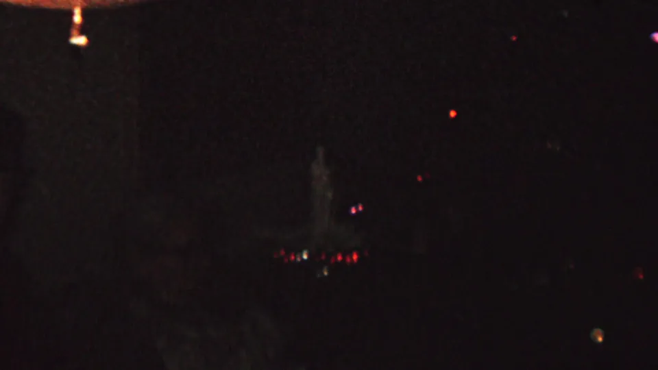 1962 8mm frame from St. Paul showing a dim nighttime skyline, scattered colored lights, and barely visible foreground or balcony-area shapes.