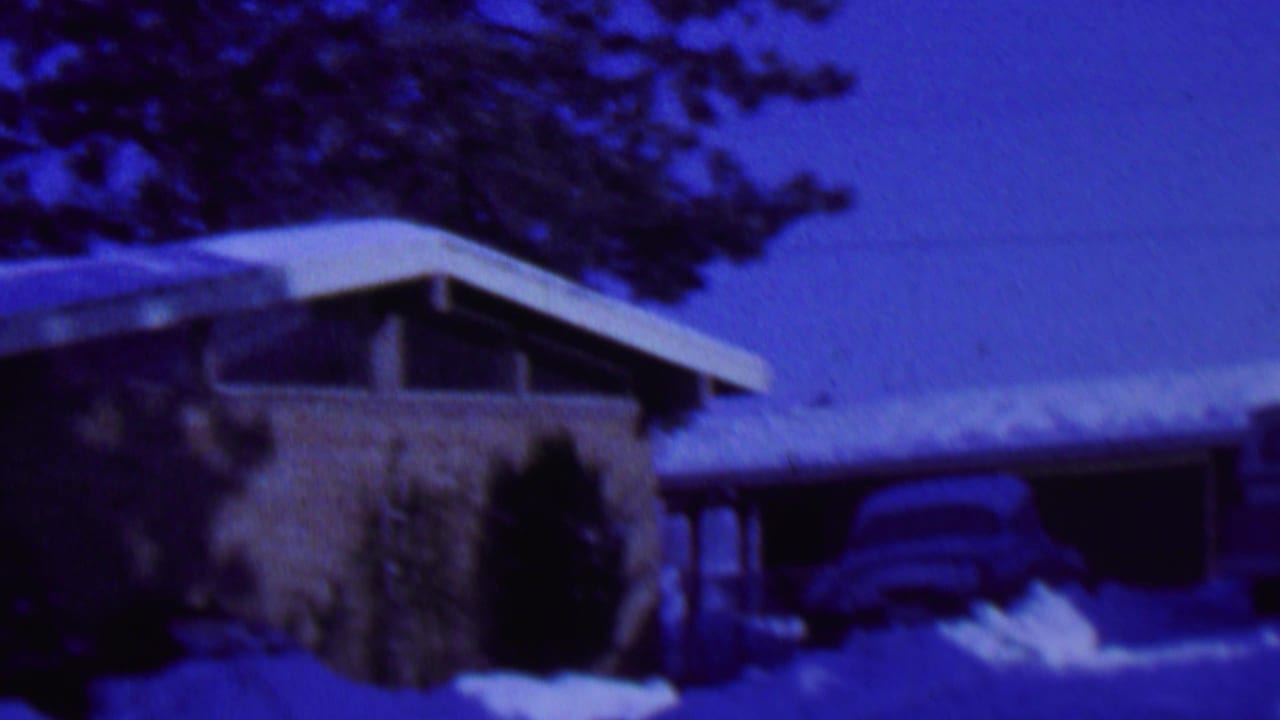 A snow-covered mid-century residential exterior in St. Paul, Minnesota, filmed in 1962 with evergreen trees and a partially visible car near the driveway.