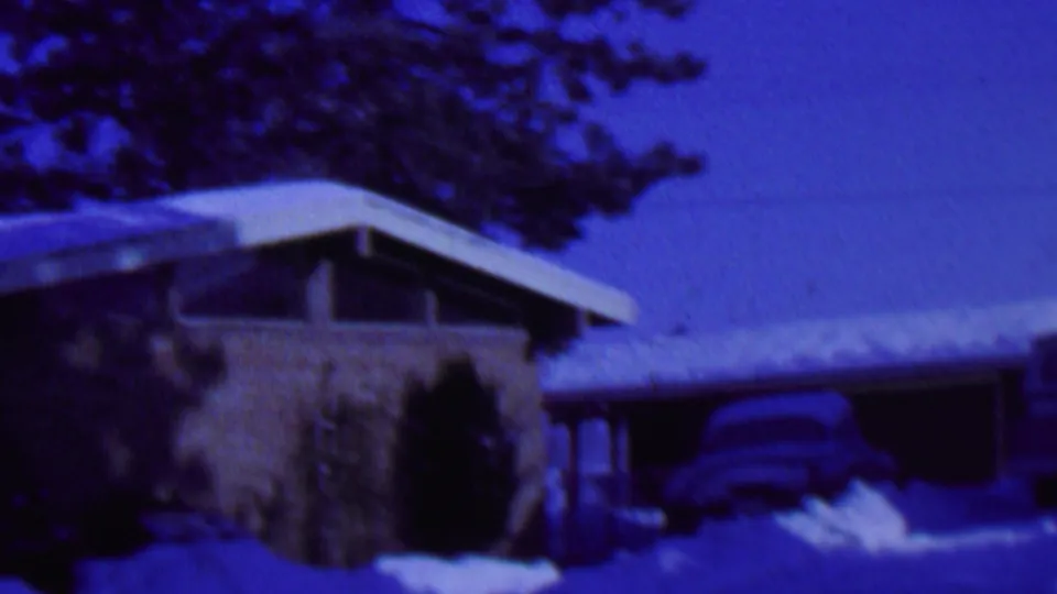 A snow-covered mid-century residential exterior in St. Paul, Minnesota, filmed in 1962 with evergreen trees and a partially visible car near the driveway.