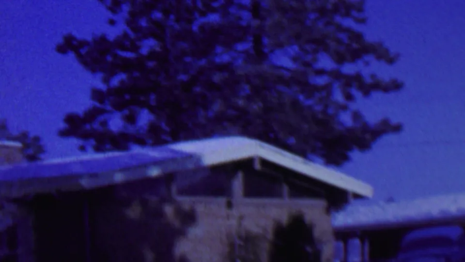 A handheld 8mm view of a snow-covered residential facade in St. Paul, Minnesota, with a flat roofline, brick wall, trees, and heavy blue film color cast.