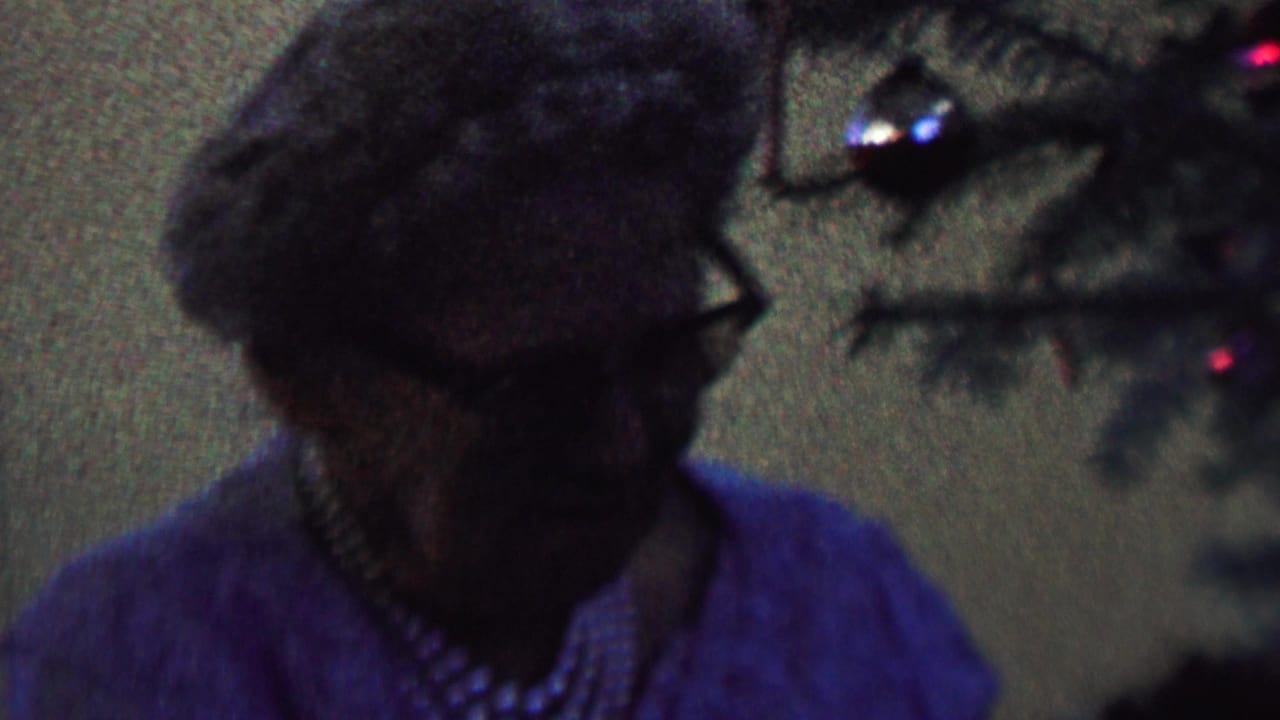 Woman in blue sweater turns beside Christmas tree ornaments.