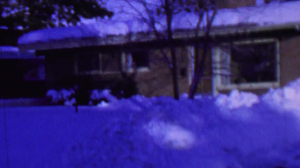 Snow blankets the yard, roof, and shrubs around a suburban house exterior, matching the supplied St. Paul, Minnesota winter holiday home-movie context.