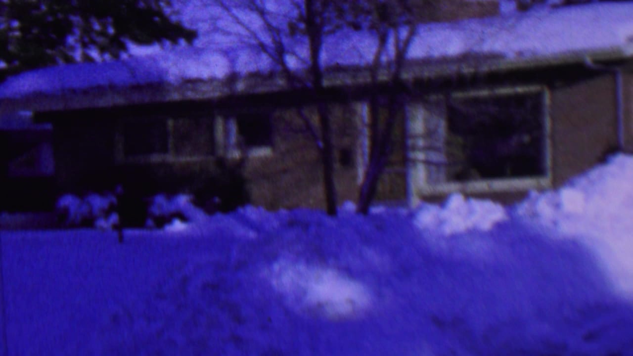 1962 St. Paul, Minnesota home-movie frame showing a snow-covered single-story brick house with bare trees and blue-purple winter shadows.