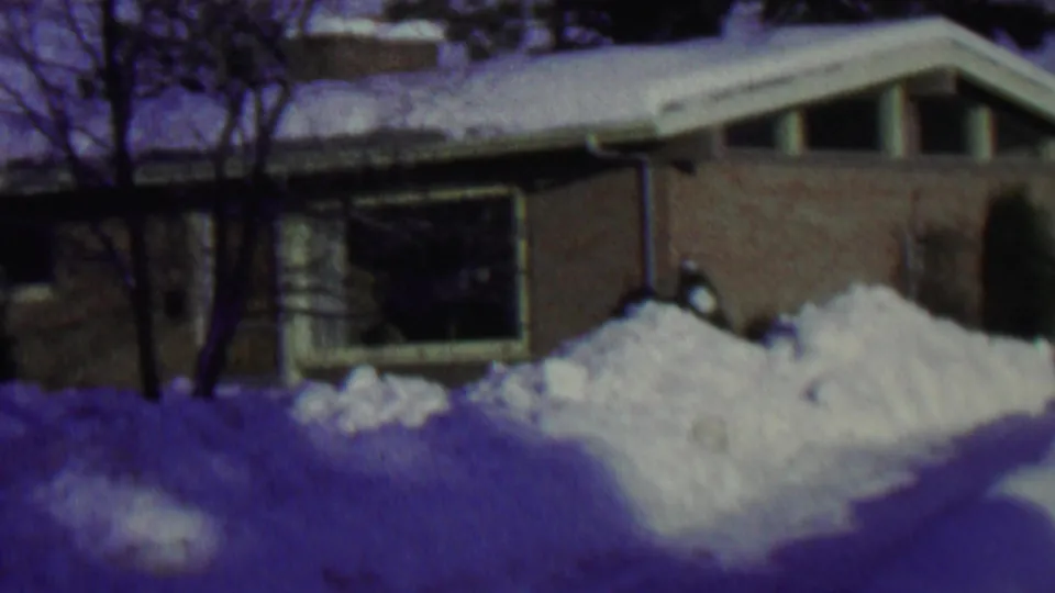 1962 St. Paul, Minnesota winter frame showing a low brick suburban house, broad front window, bare trees, and bright piled snow in front.