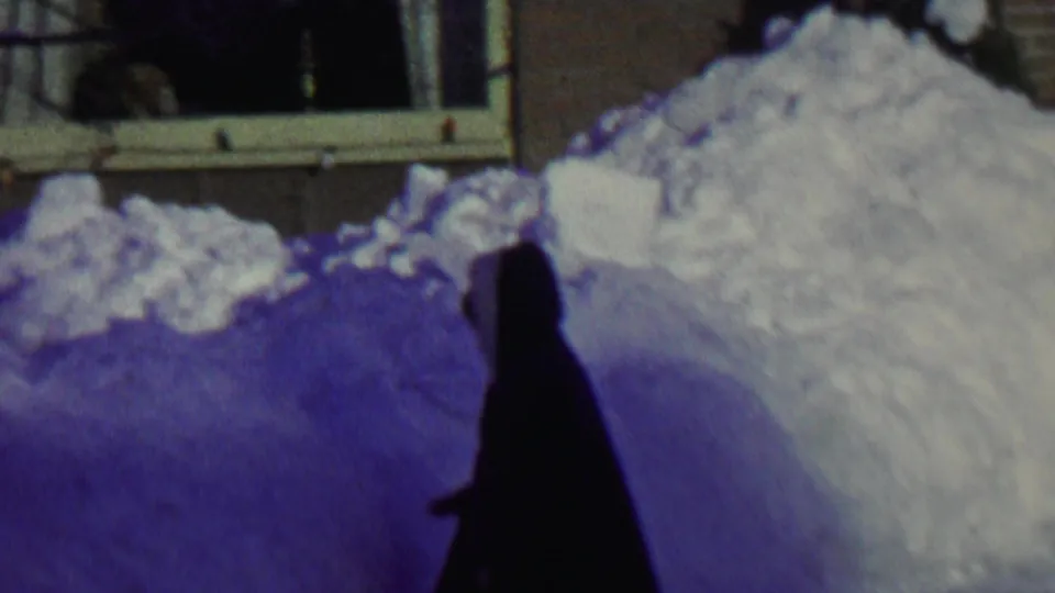 In 1962 St. Paul home-movie footage, a dark hooded figure stands near deep piled snow outside a residential window.