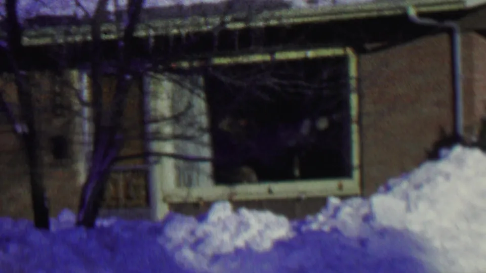 A residential window, tree trunk, and deep snowbank fill the frame as the 1962 St. Paul winter yard scene ends.