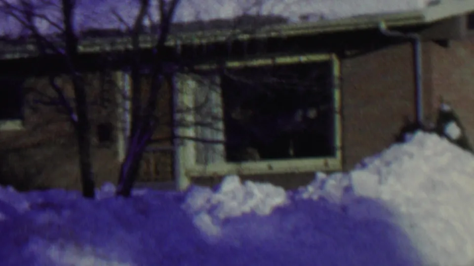 1962 St. Paul home-movie frame showing a snowbound single-story brick house, bare trees, roof snow, and a large shaded front window.