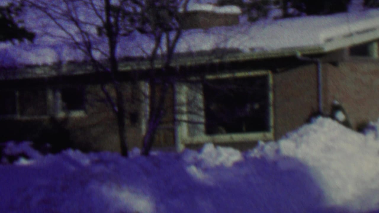 1962 St. Paul winter frame with a low brick house partly obscured by snowbanks, bare trees, and a shaded window.