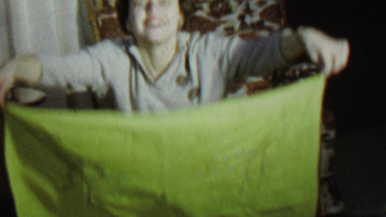 Woman in a light sweater holds a green sheet across her body indoors.