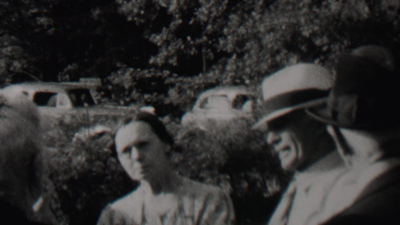 In this 1937 Trenton, New Jersey home-movie frame, adults in dress clothing appear outdoors near leafy shrubs with rounded automobiles parked behind them.