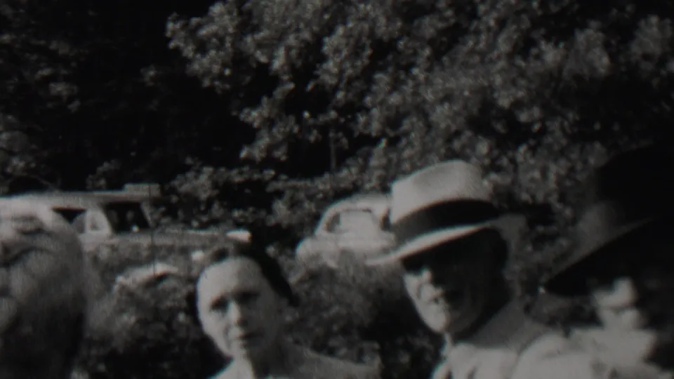 Several adults, including women in hats and a light dress, stand close to the camera in a soft black-and-white 1937 outdoor home-movie frame.