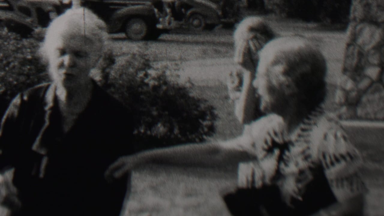 Elderly woman standing outdoors while another person gestures nearby.