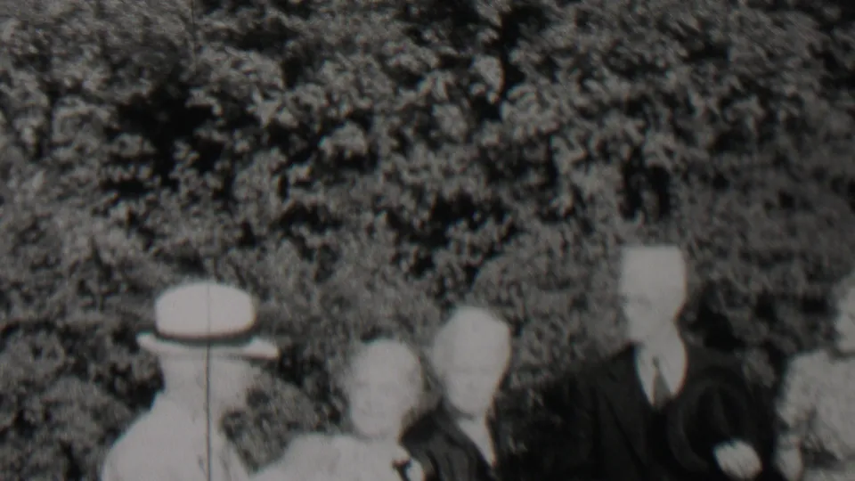 1937 Trenton, New Jersey frame showing several adults at an outdoor gathering, including white hats, a suited man, hedges, and leafy trees.