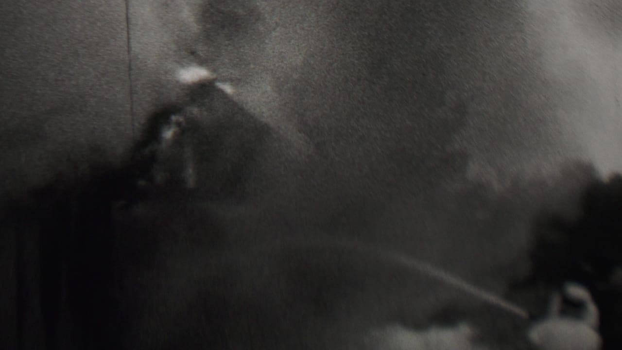 In supplied 1937 Trenton, New Jersey home-movie footage, smoke billows near a dark structure while a hose stream cuts across the scene.