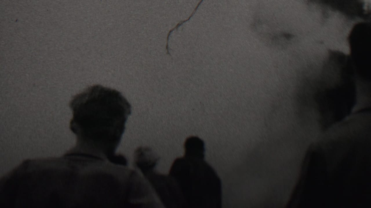 A rear view of a man and nearby onlookers watching a dark smoke or fume cloud in archival 8mm footage associated with Trenton, New Jersey, 1937.