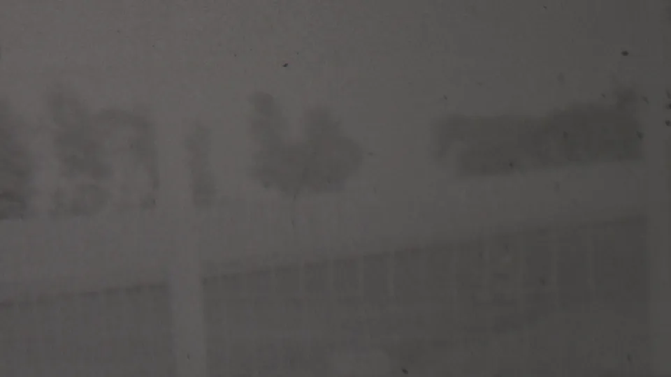 Very dark 1937 8mm home-movie frame from the described Trenton, New Jersey clip, showing an indistinct outdoor dirt-track area with faint trees or structures in the distance.