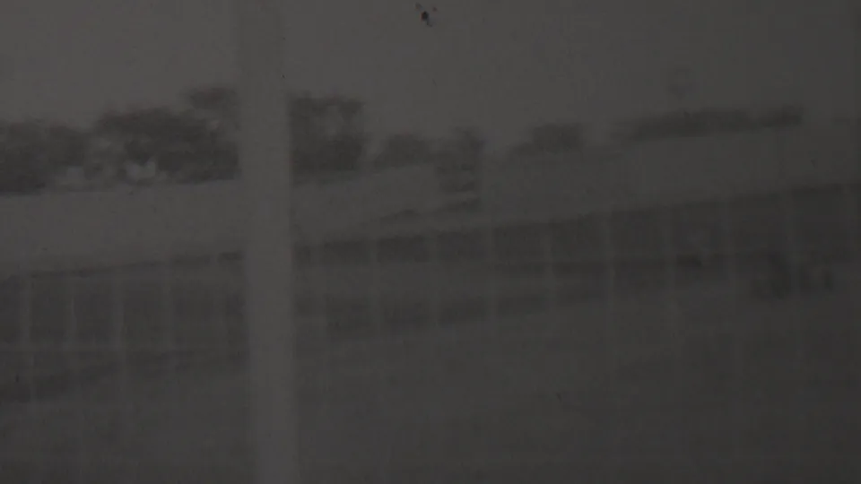 Dark 1937 home-movie frame that appears to show the dirt track with a low blurred form near the lower left, consistent with the described small racer passing through the scene.