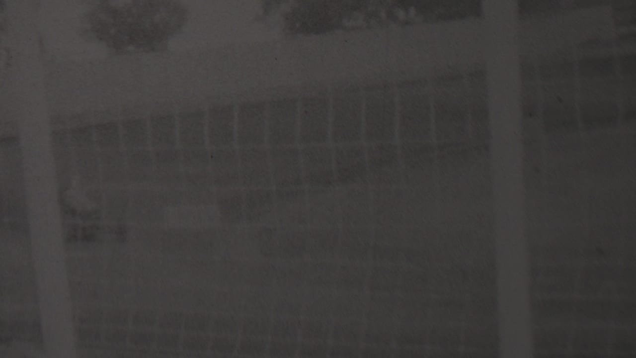 Soft 1937 Trenton home-movie frame showing a faint outdoor track area with trees, a low structure or fence line, and heavy film grain.