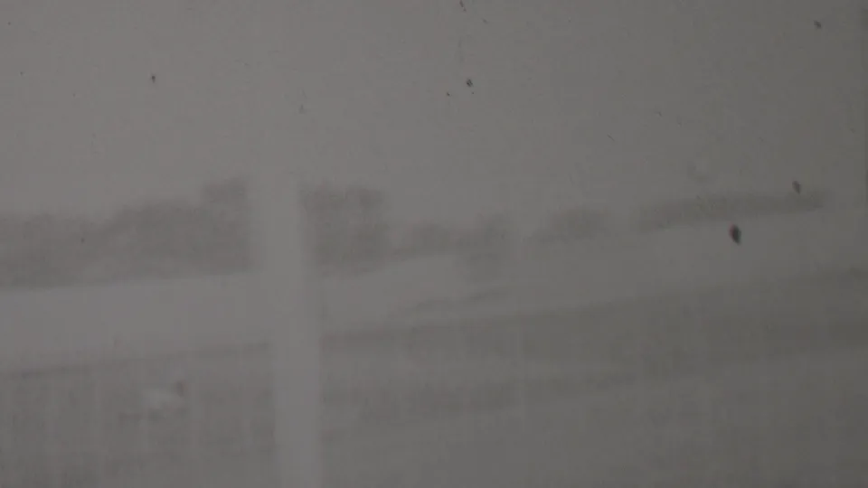 A heavily obscured 1937 home-movie frame from the supplied Trenton, New Jersey clip shows faint outdoor structures and trees through grain, dust, and low contrast.