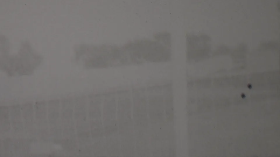 This 1937 home-movie frame from the supplied Trenton clip shows a very faint outdoor scene with a darker block-like form, pale ground, and heavy grain and dust.