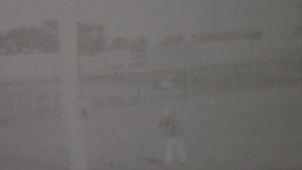 A small light-clothed figure appears near the lower right of this obscured 1937 Trenton home-movie frame, with faint outdoor structures and trees behind them.