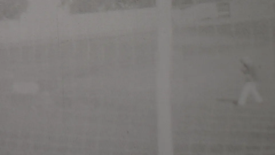 Distant rider appears on a bright, soft-focus black-and-white frame, with the track, low fencing, and background shapes barely resolved by the 8mm scan.
