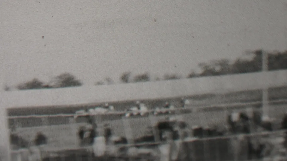 Black-and-white 1937 home-movie frame showing a distant race-track view in the Trenton, New Jersey clip, with cars, spectators, fencing, and trees across the background.