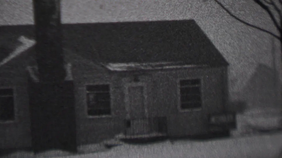 Final black-and-white frame of the snowy residential exterior, with the chimney centered and the front door and windows visible.