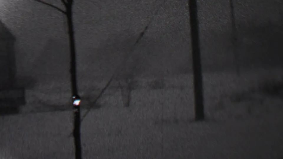 Grainy black-and-white 1937 Trenton home-movie frame showing a dark snowy yard, bare trees, and indistinct residential structures beyond.