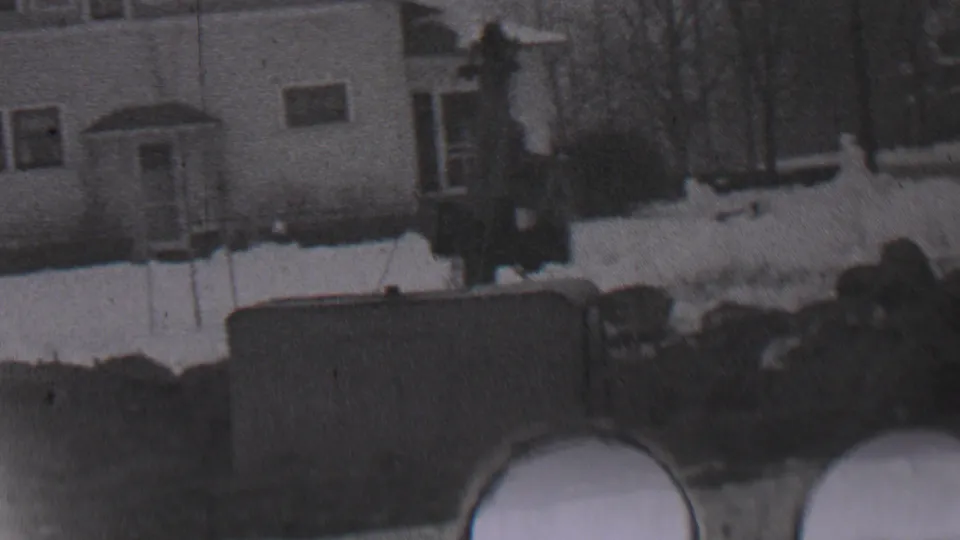 1937 Trenton winter home-movie frame showing a snow-covered residential exterior with a porch, windows, bare trees, and dark yard objects in the foreground.